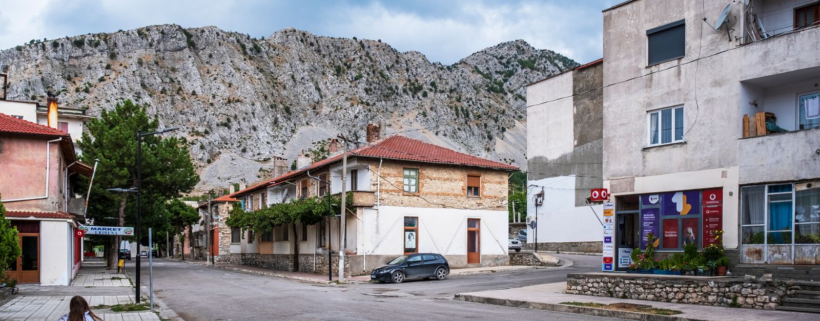 Picturesque village street in Albania with classic architecture framed by rugged mountains.