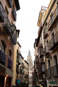 A charming street view in Toledo, Spain, showcasing traditional architecture and a cathedral spire.