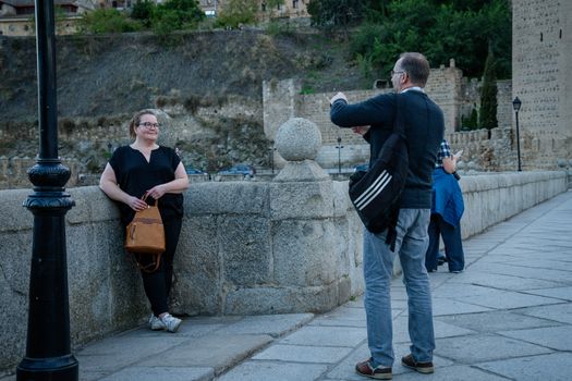 A woman poses for a photo at a historic site in Toledo, Spain, with a man taking her picture.