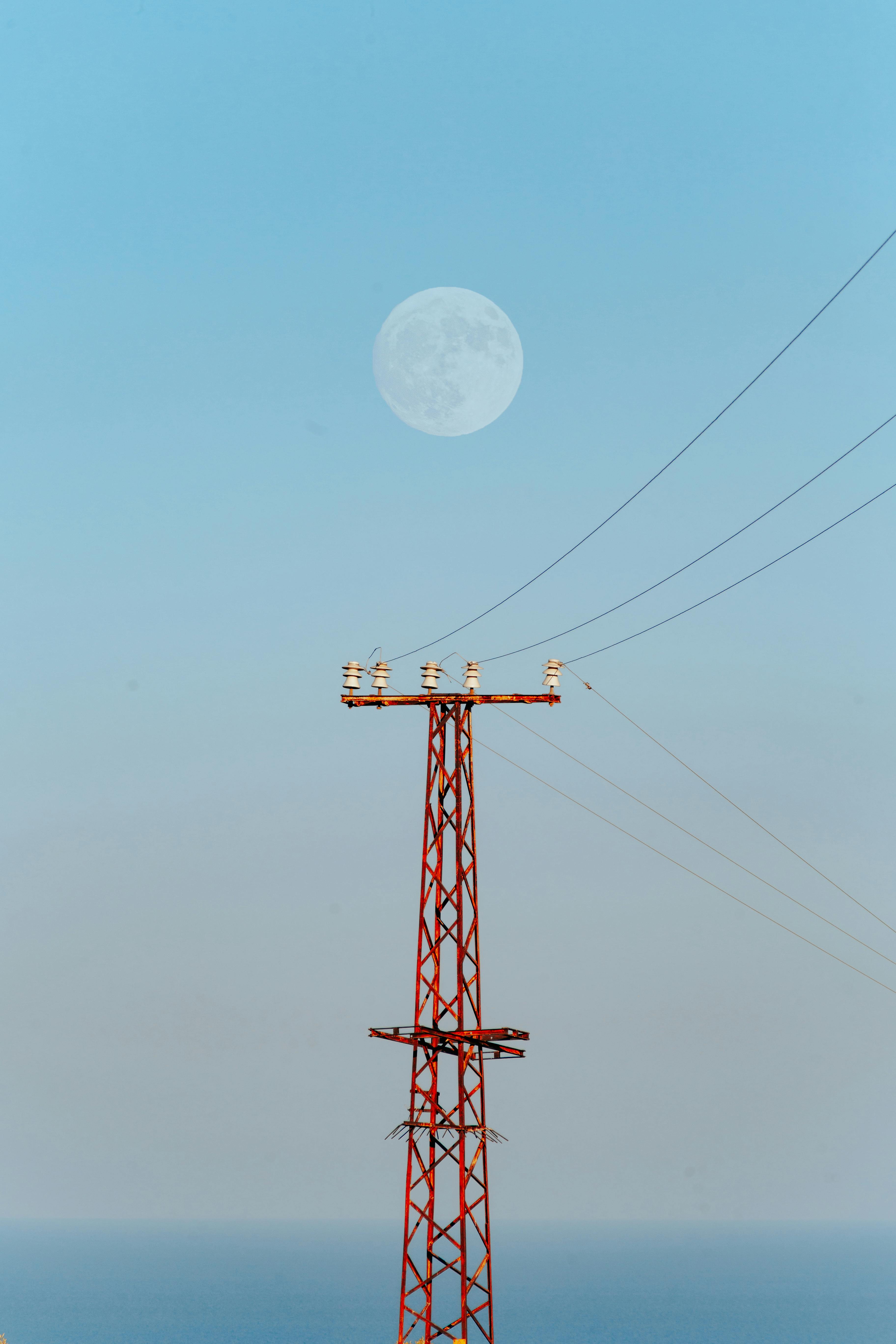 A serene view of a full moon over a red transmission tower in Adana, Türkiye.