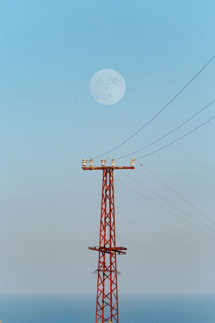 A serene view of a full moon over a red transmission tower in Adana, Türkiye.