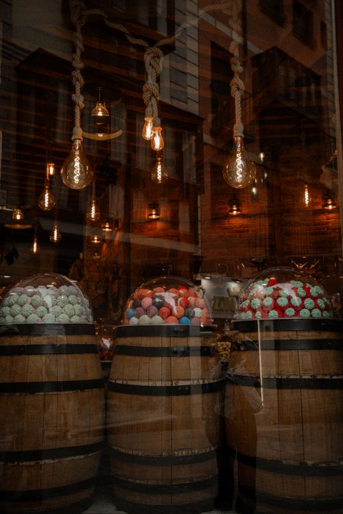 Free Rustic candy shop display featuring colorful sweets in wooden barrels and vintage lighting. Stock Photo