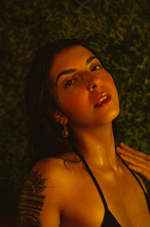 Free A captivating portrait of a woman with a tattoo, highlighted by warm lighting and moody ambiance. Stock Photo