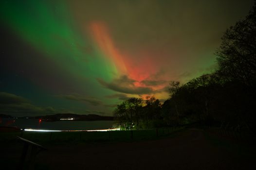 Vibrant display of Aurora Borealis over a tranquil lake surrounded by trees during a clear night.