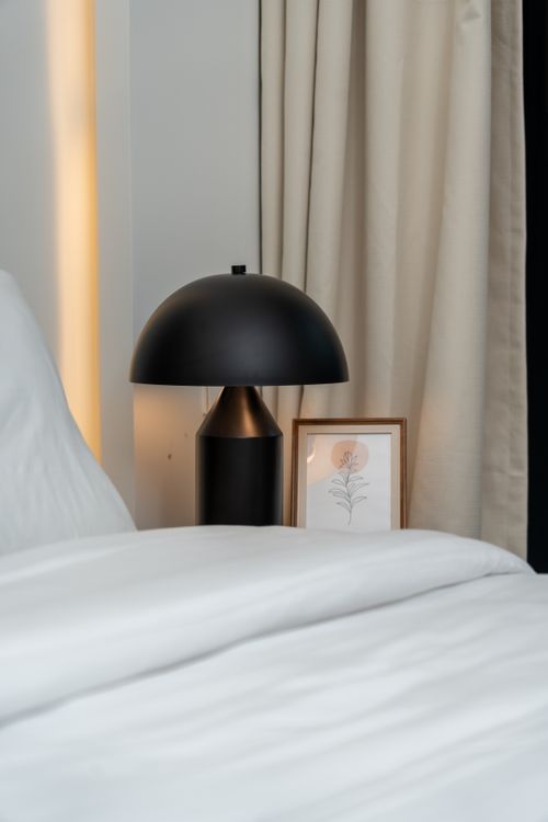 Free A sleek black lamp on bedside table, elegant and modern, in a cozy bedroom setting. Stock Photo