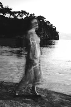 Black and white blurred figure walking along a serene seaside landscape, artistic impression.