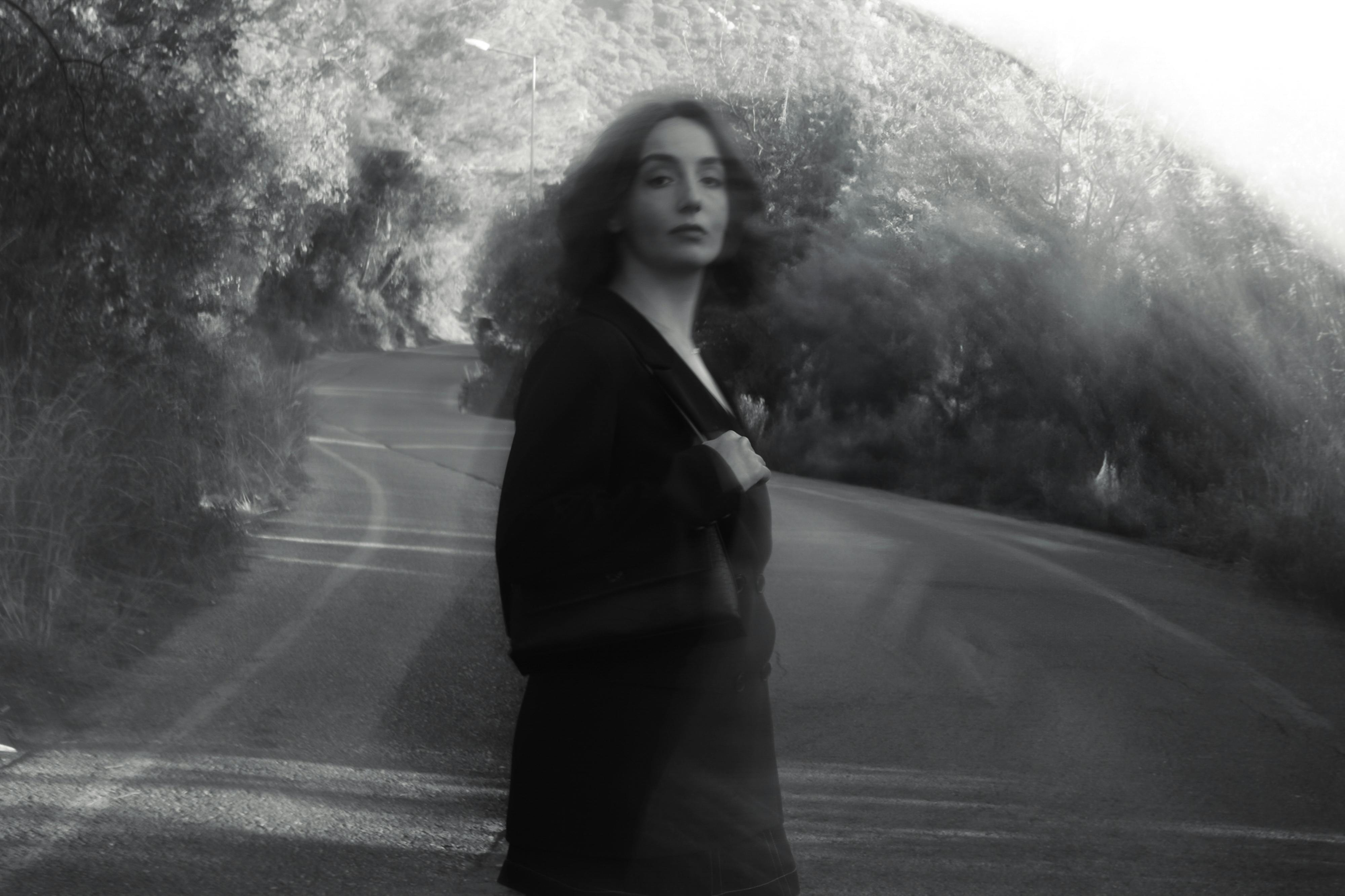 A blurred black and white image of a woman on a winding road, evoking mystery and solitude.