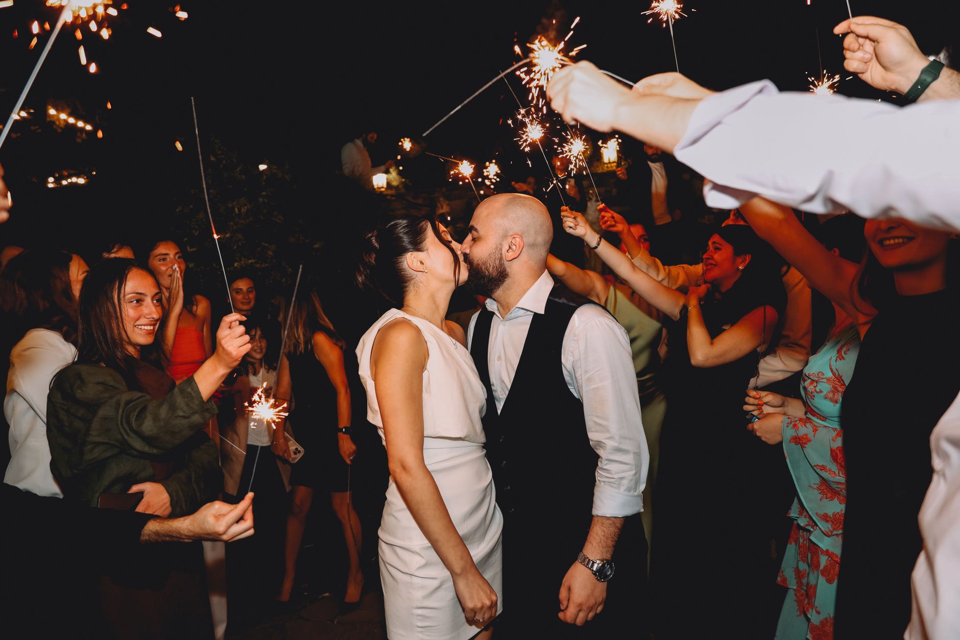 best wedding planner in cairo — Couple sharing a kiss at night surrounded by sparklers and guests, creating a festive wedding