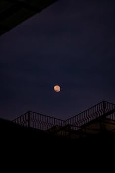 A captivating view of the half moon against a dark Jakarta night with silhouetted structures in the foreground.