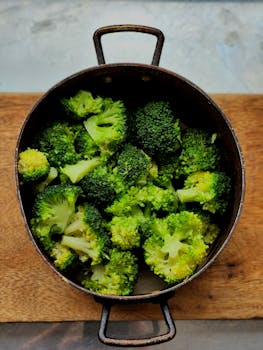 A top view of fresh broccoli florets in a rustic pot on a wooden board.