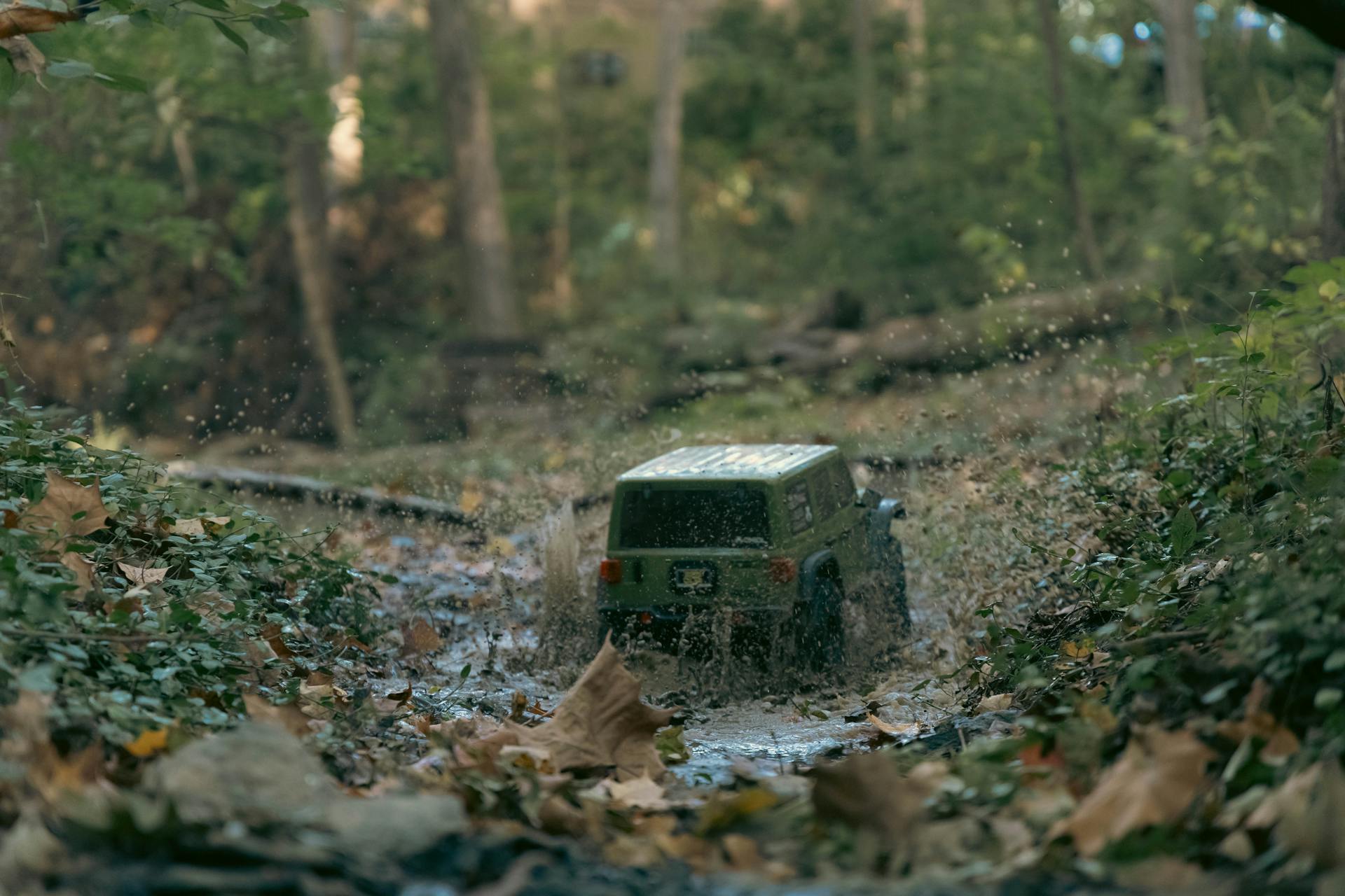 Scale model SUV splashes through muddy forest path, showcasing off-road adventure.