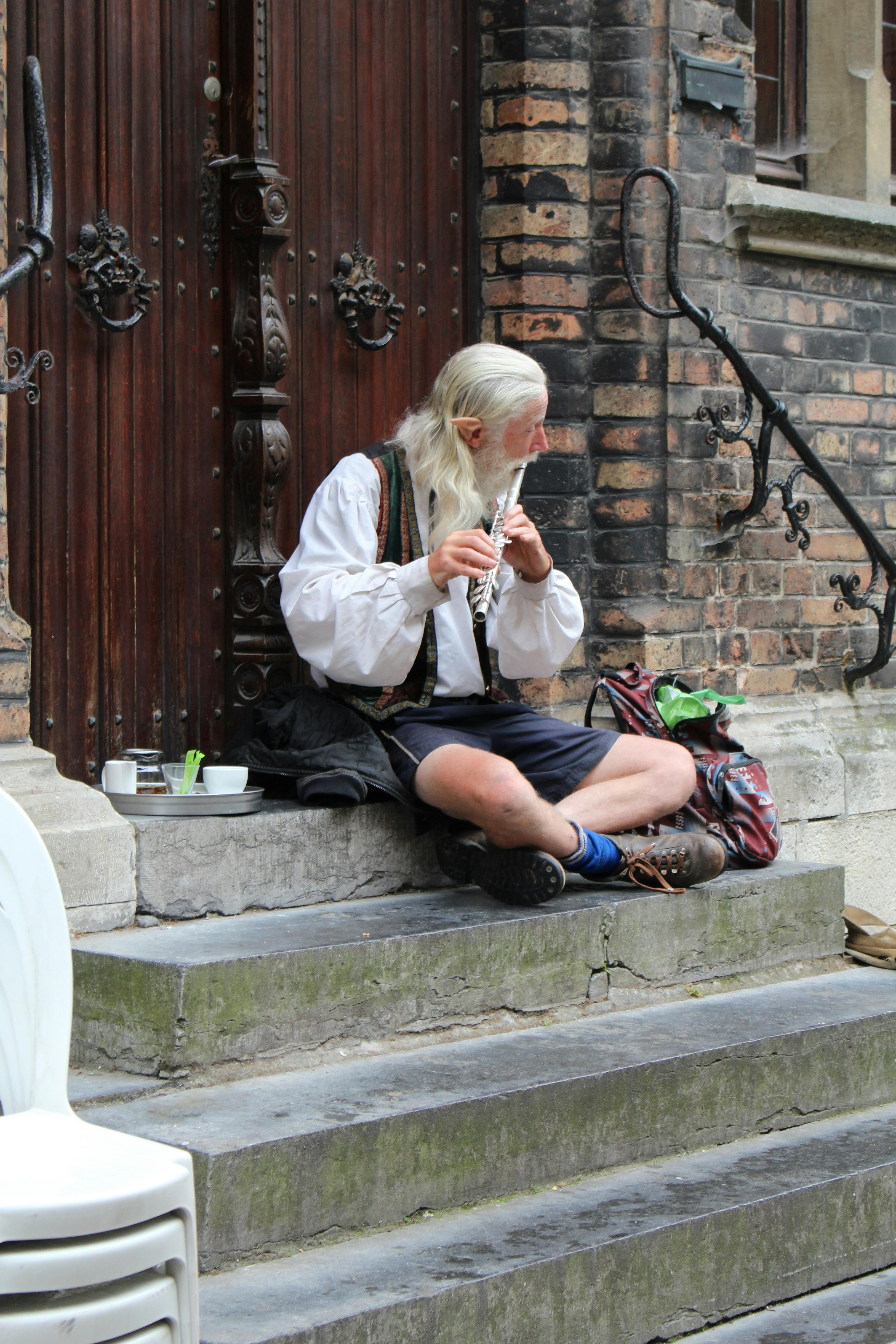 A bearded street musician plays the flute on stone steps in Bruges, Belgium.