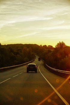 A beautiful sunset view on a winding road with a car driving through lush greenery.