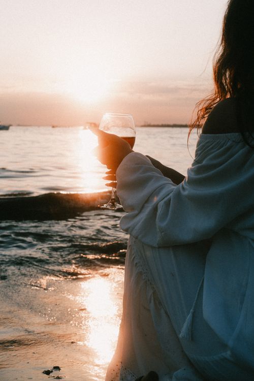 Free A serene scene of a woman at sunset, sipping wine by the beach. Perfect for lifestyle and travel themes. Stock Photo