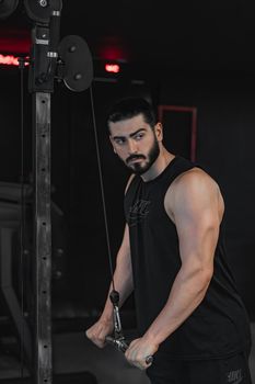 Focused young man using cable machine for strength training in a dimly lit gym.