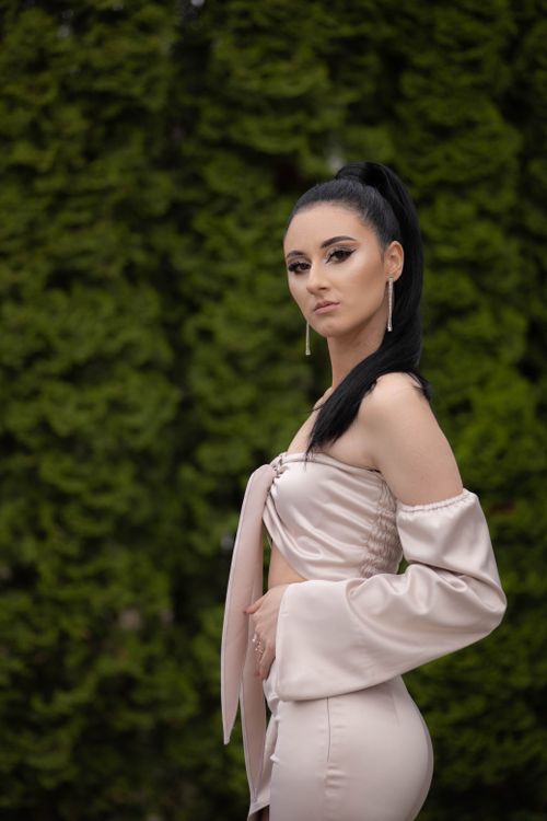 Free Elegant woman in a chic outfit posing outdoors against lush greenery, exuding confidence and style. Stock Photo