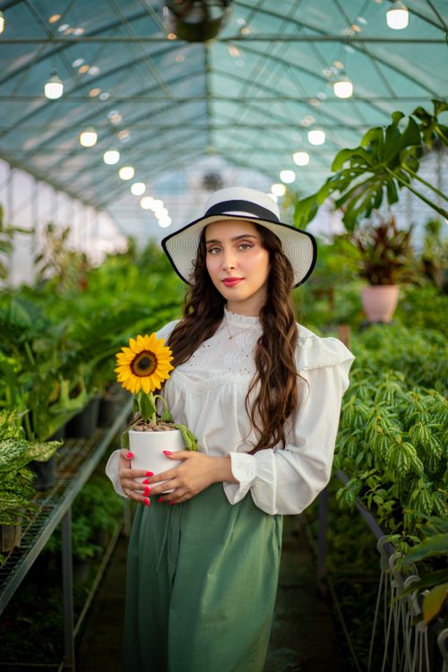 Free Elegant woman in a hat holding sunflower plant in greenhouse. Stock Photo