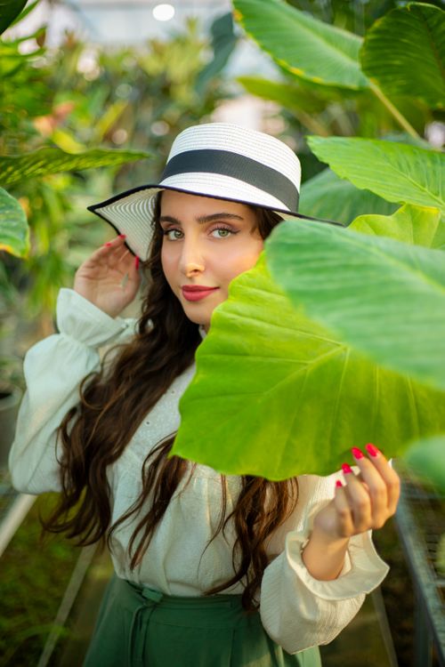 Free Elegant woman with long hair in a botanical garden, holding a large leaf. Stock Photo