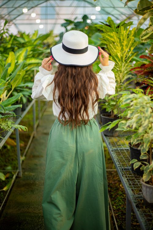 Free A woman in stylish attire explores a lush greenhouse filled with vibrant plants. Stock Photo