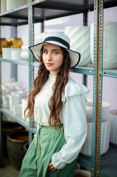 Chic woman in fashionable attire with hat, posing in an indoor greenhouse.