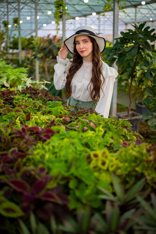 Free Young woman in a greenhouse surrounded by vibrant green plants. Stock Photo
