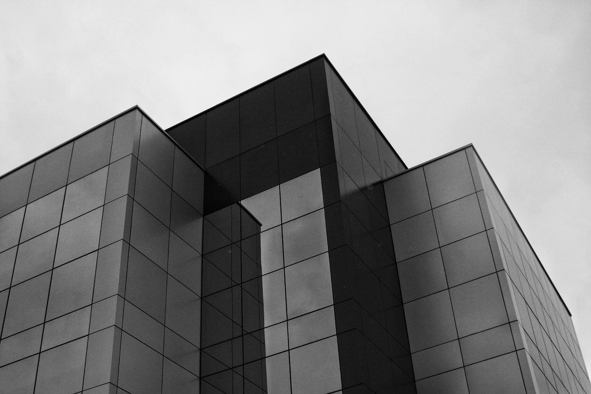 Black and white photo of a modern glass building with geometric design against a cloudy sky.