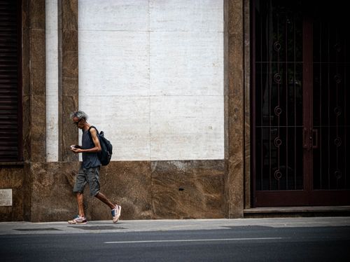 Free A man walks near a building in São Paulo, Brazil, immersed in his smartphone. Stock Photo