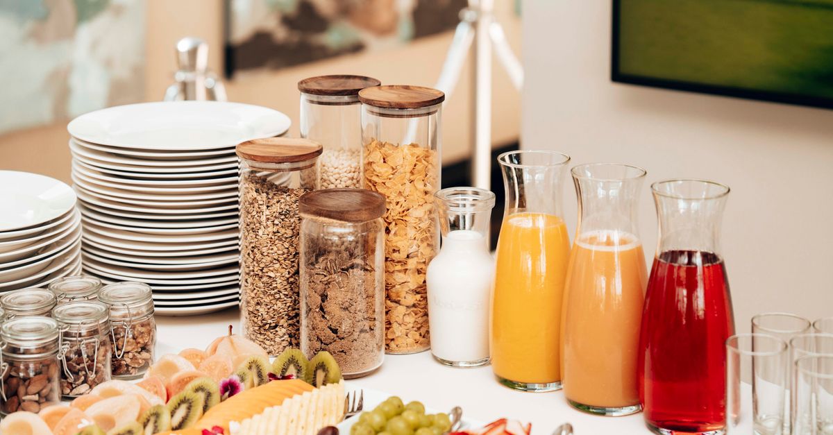 Uma variedade de itens de café da manhã, incluindo cereais, frutas frescas e sucos dispostos em uma mesa de buffet.