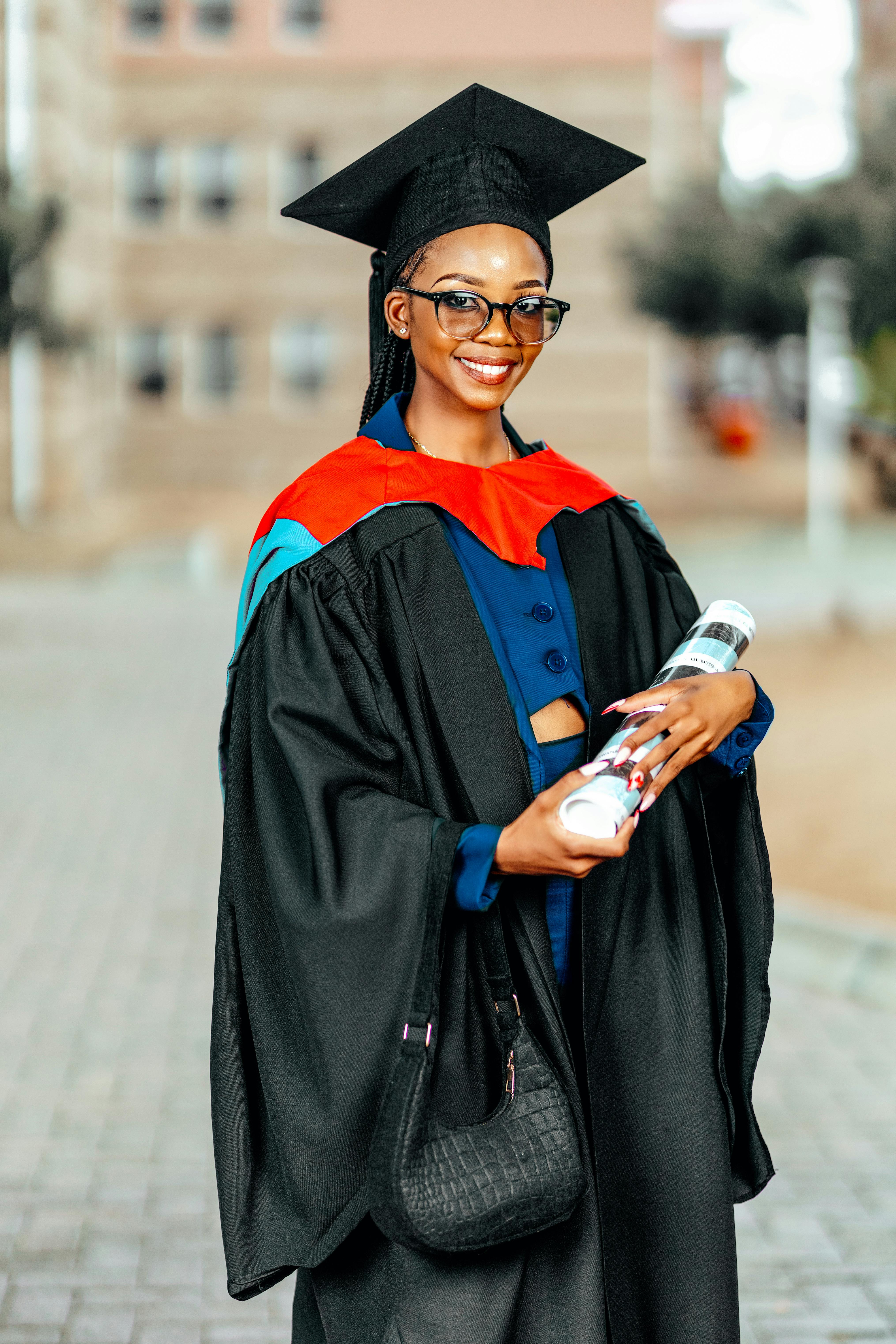 Smiling graduate woman in cap and gown holding diploma outdoors.