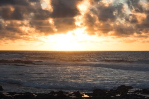 Free Breathtaking sunset over Lanzarote's rocky coastline with dramatic clouds and ocean waves. Stock Photo