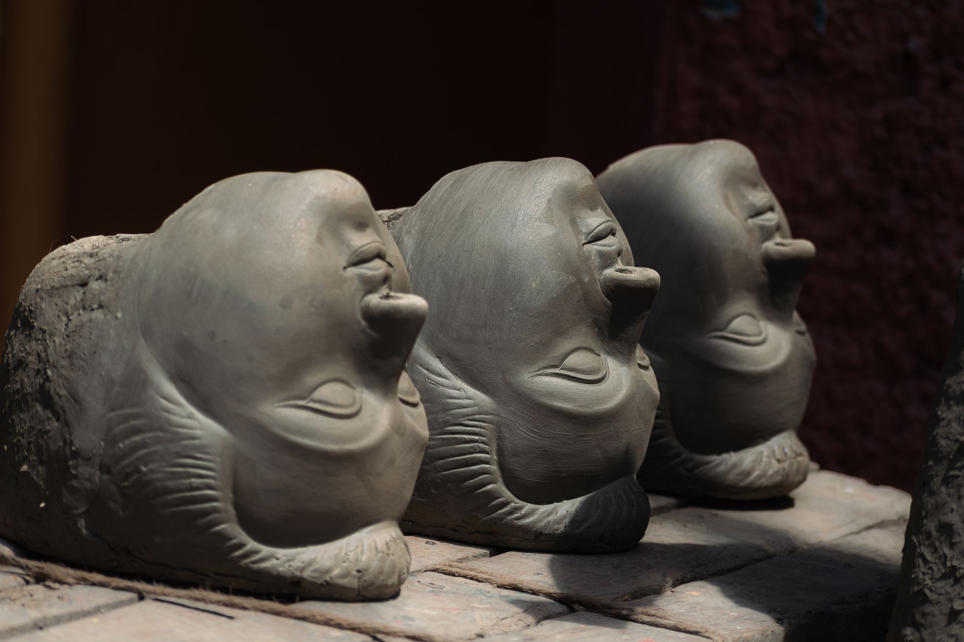 Three unfinished clay heads for Durga figures in a Kolkata workshop, bathed in sunlight.