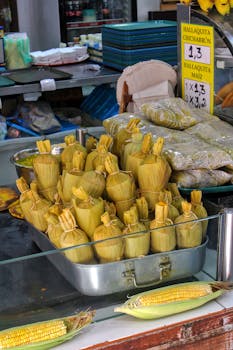 Delicious hallaquitas and fresh corn displayed at a vibrant street food market.