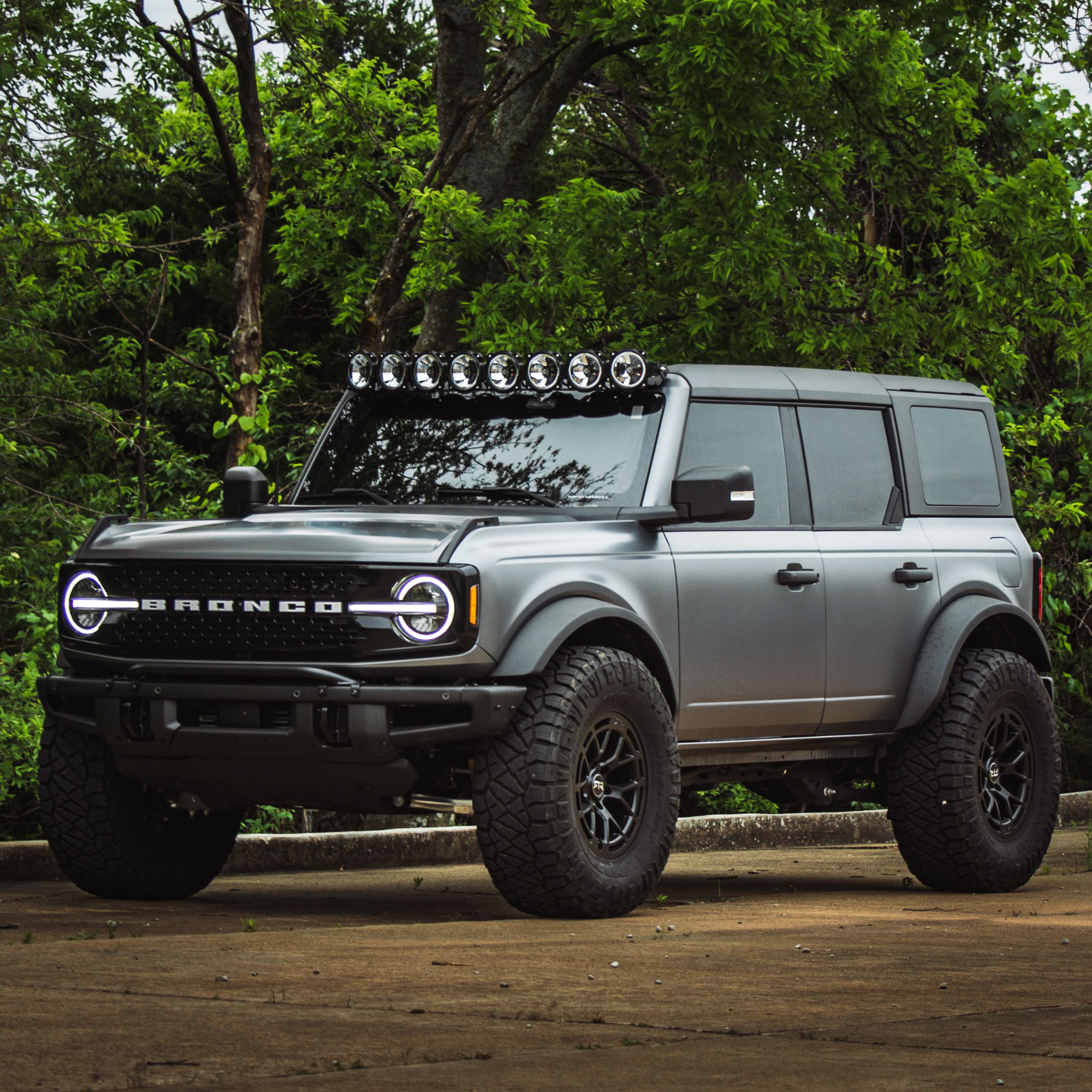 Dramatic shot of a Ford Bronco SUV with off-road tires in Tulsa's lush greenery.