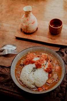 Japanese curry rice with breaded chicken served with sake set on a rustic wooden table.