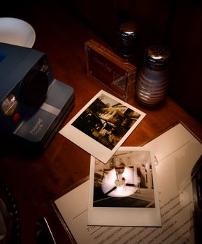 A vintage Polaroid camera on a table with instant photos and salt and pepper shakers.