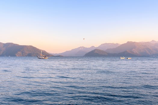 Serene ocean scene with boats against mountain backdrop in the soft light of sunrise.