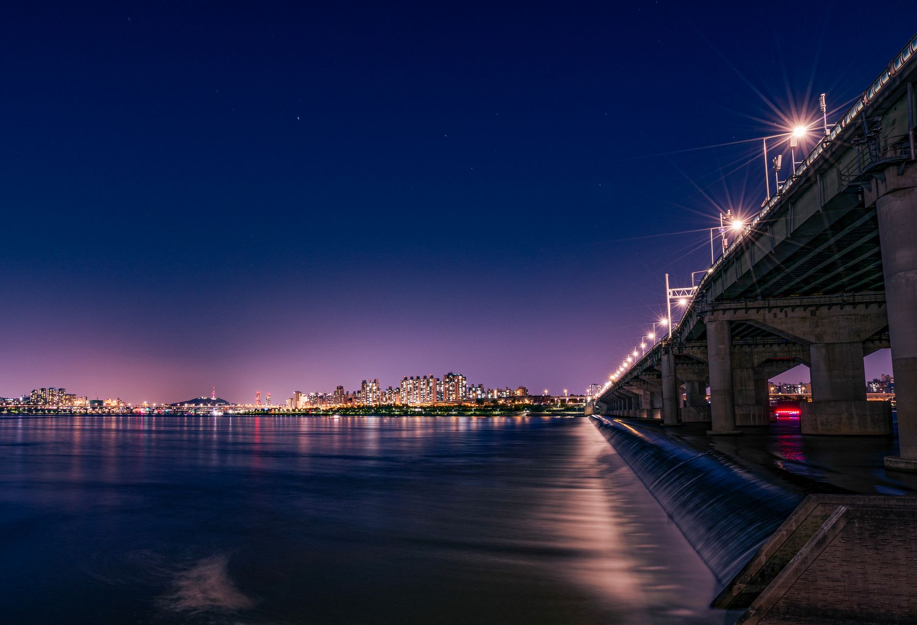 Vibrant night view of Seoul with illuminated bridge and city skyline reflecting on Han River.