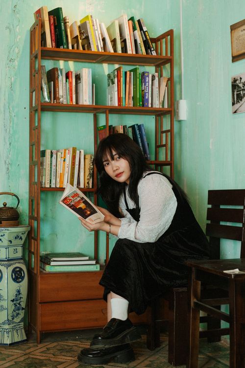 Free Portrait of a young woman reading in a quaint Hanoi café with vintage décor and bookshelves. Stock Photo