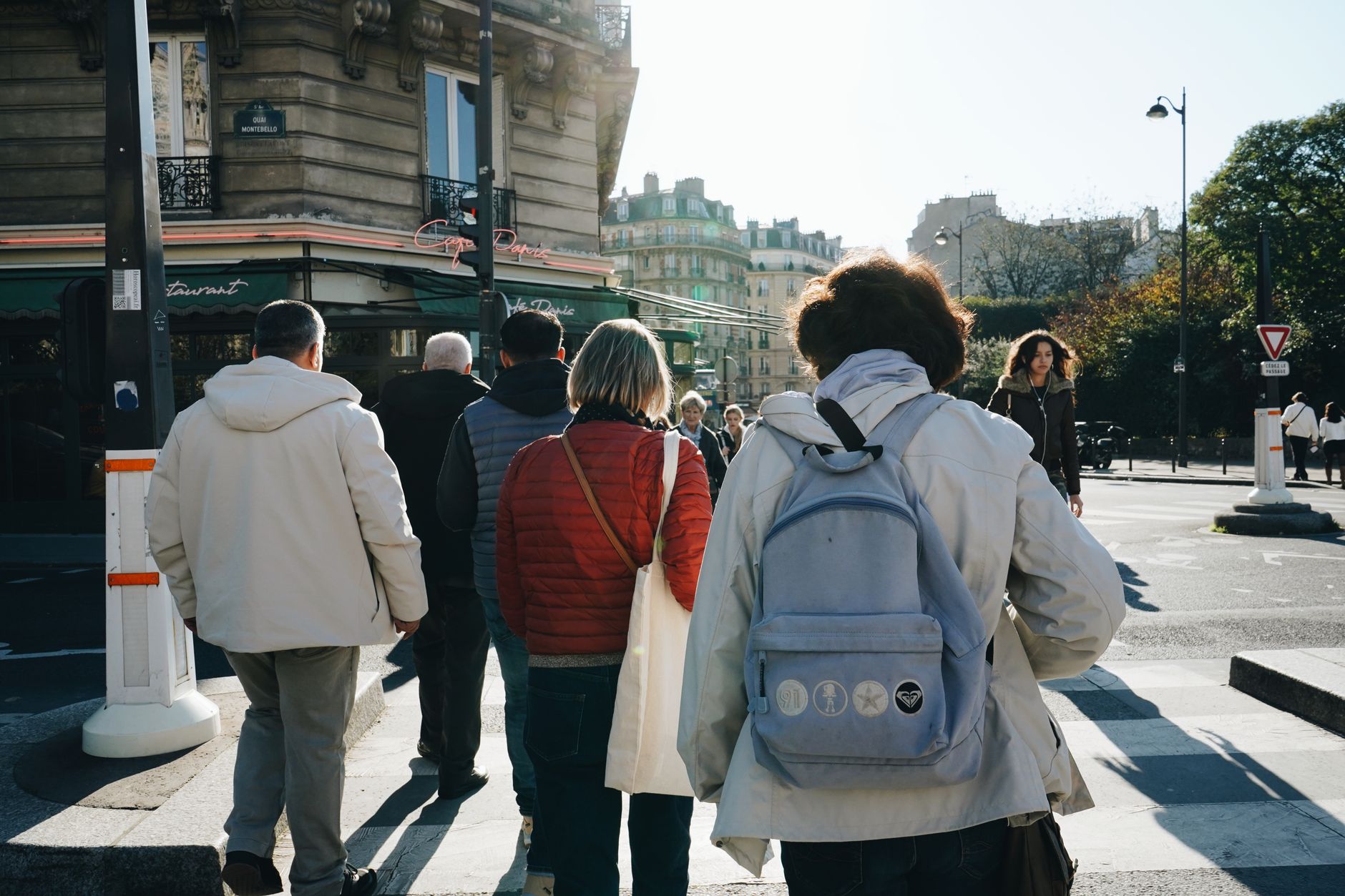 Candid scene of pedestrians crossing a Parisian street under the autumn sun.