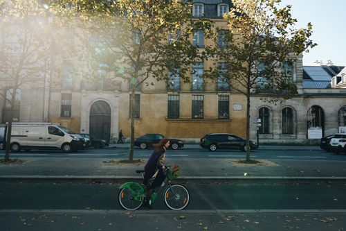 Free Woman cycling in the city during a sunny autumn day, with lens flare and buildings. Stock Photo