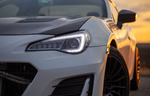 Free Detailed shot of a sports car during a vibrant sunset, showcasing sleek design and headlights. Stock Photo