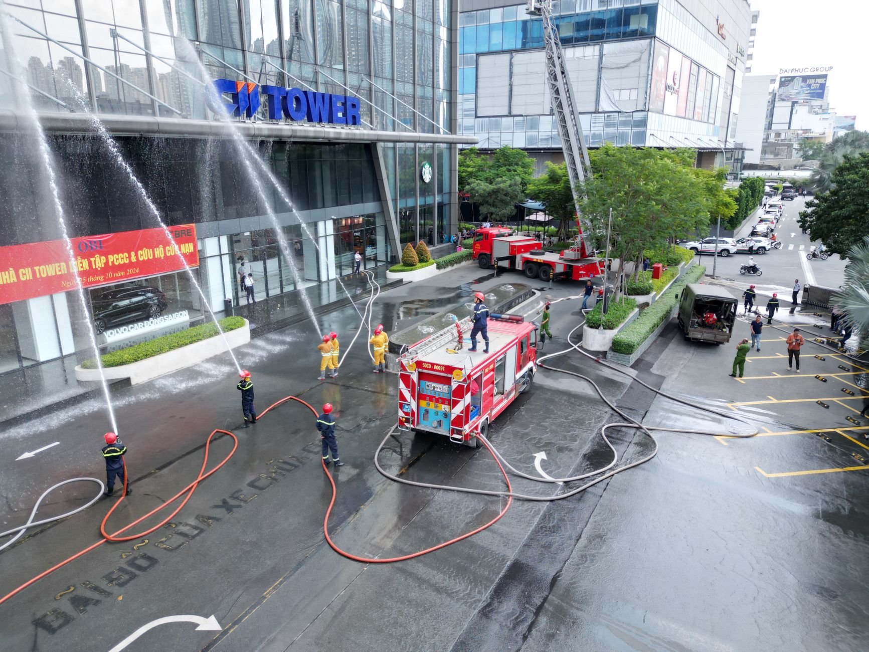 Firefighters conducting a drill with hoses and trucks at a modern office building.