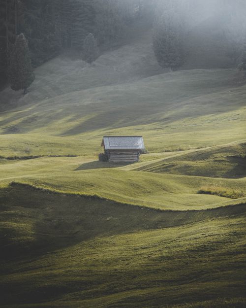 Free Solitary cabin amidst lush green pastures and misty hills in Trentino-Alto Adige. Stock Photo