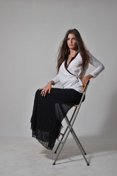 Stylish portrait of a woman seated on a chair in monochrome outfit, exuding elegance.