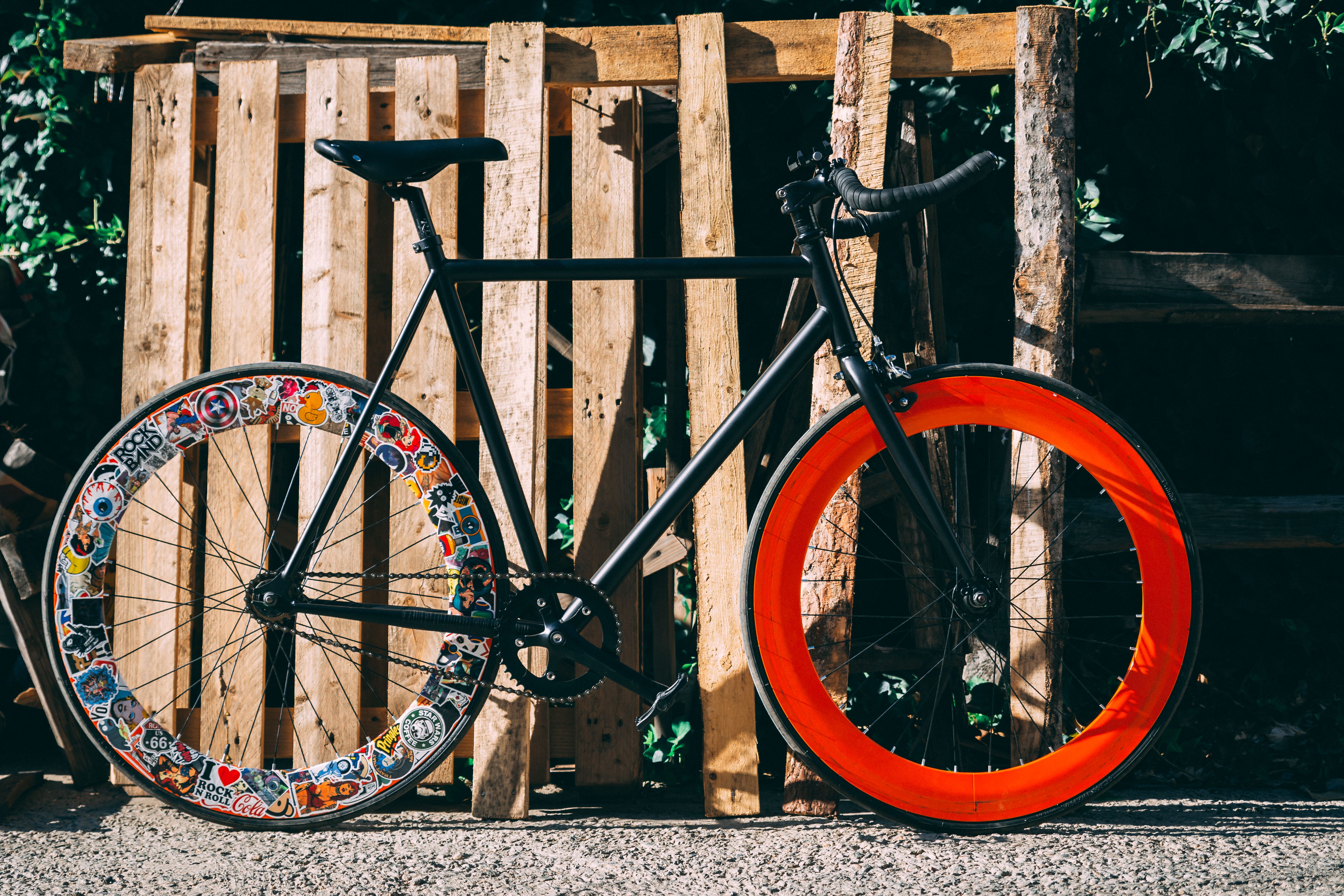 Unique bicycle with sticker-covered wheel and orange rim parked outdoors.