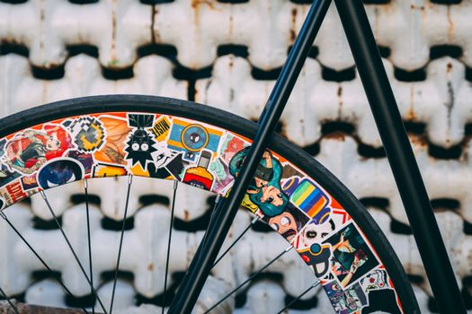 Close-up of a bicycle wheel adorned with vibrant stickers against a textured backdrop.