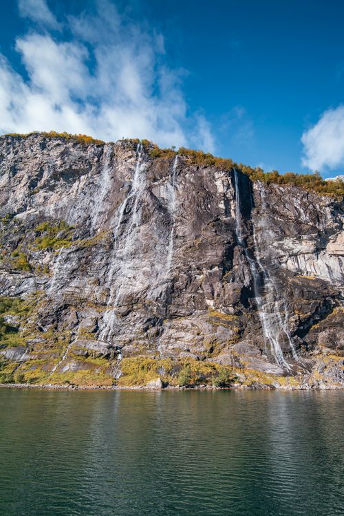Free Stunning Norwegian waterfall flowing down rocky cliffs under a clear blue sky. Stock Photo