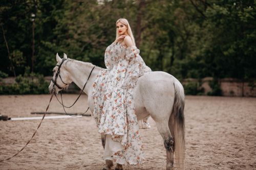 Free Elegant woman wearing a floral dress riding a white horse in a serene outdoor setting. Stock Photo