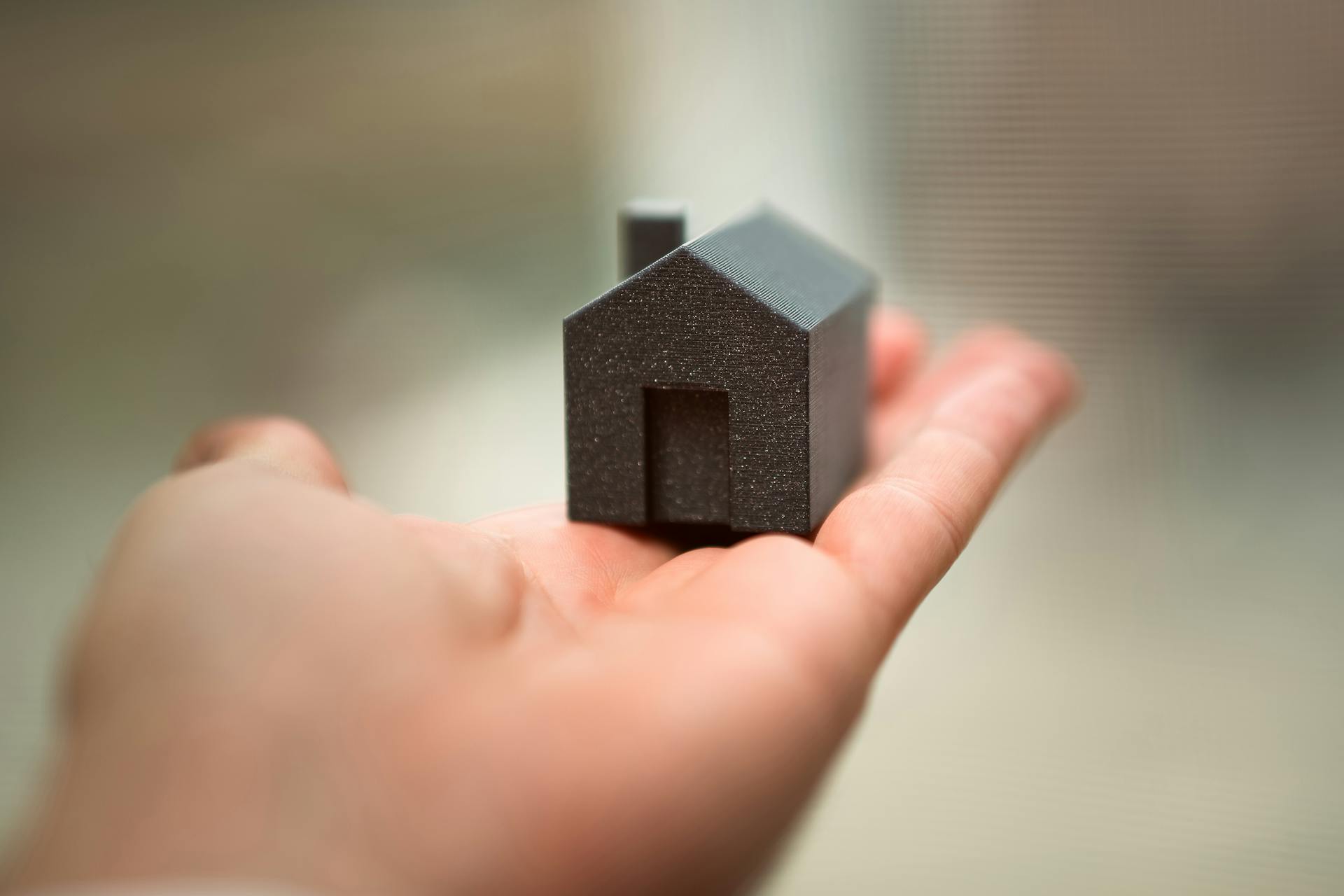 Close-up of a hand holding a miniature house model representing real estate concepts like buying or investment.