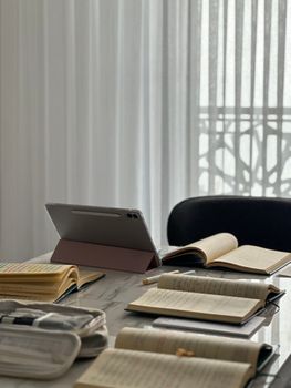 Bright study area with a tablet and open notebooks on a marble table.